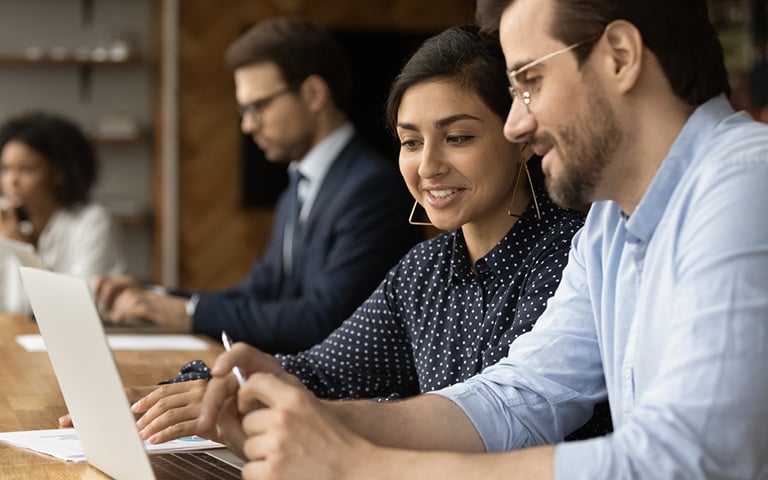 Two people smiling looking at a laptop at a desk.